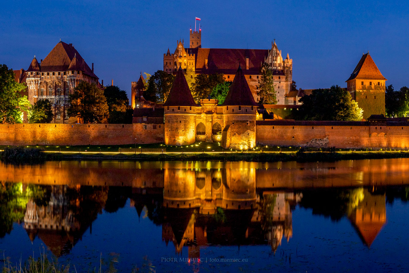 Oświetlony Zamek Malbork i jego odbicie w rzece Nogat